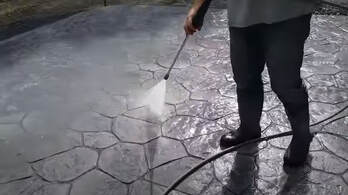 Man holding a hose spraying protective sealant on stamped concrete in Westminster, Colorado